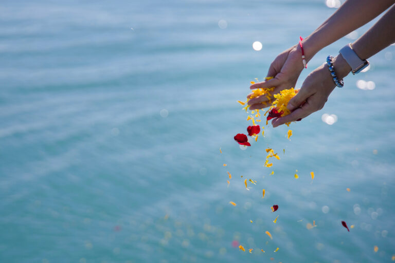 hands scattering ashes and flowers into ocean