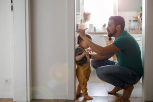 father marking toddler's height on doorframe inside family home