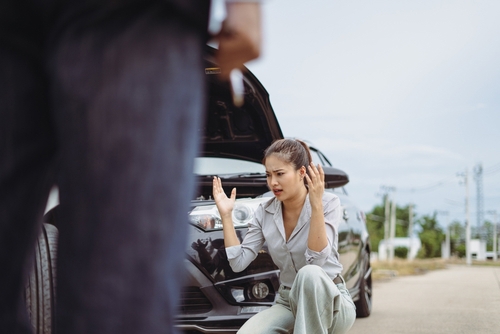 Woman sitting in car with hands on head, appearing visibly distressed
